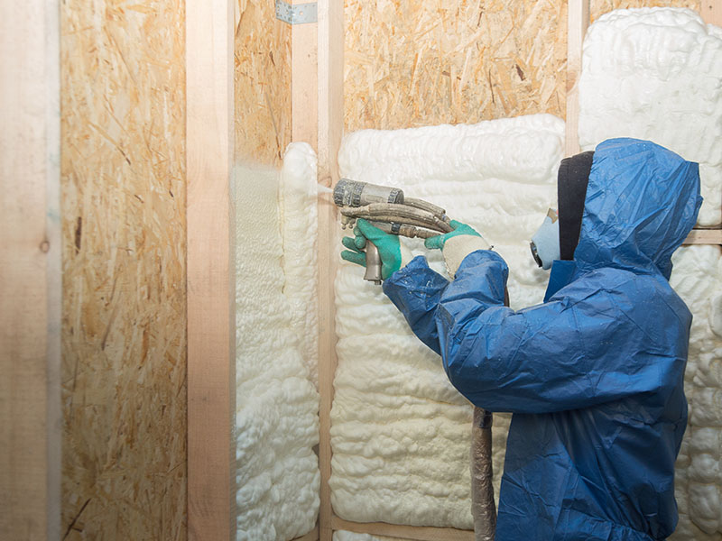 Worker spraying white foam insulation to the interior walls of a home