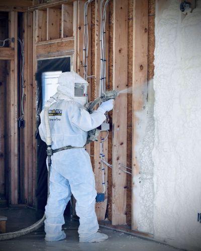 Worker spraying white foam insulation to the interior walls of a home