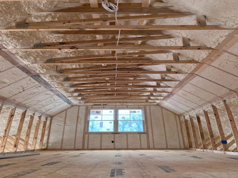 Close-up of a worker's spray gun spraying foam insulation on top of a wooden framed home