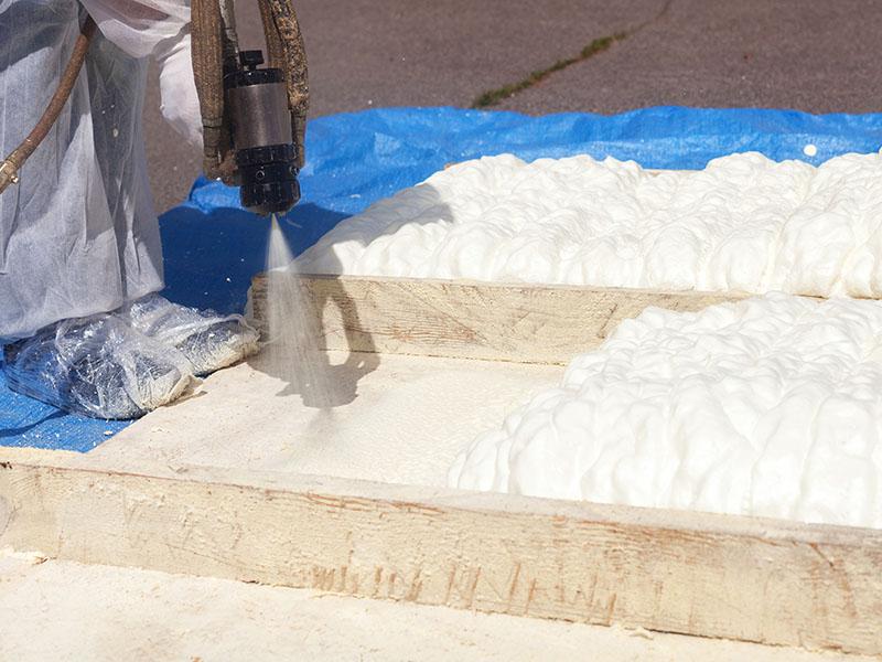 Close-up of a worker's spray gun spraying foam insulation on top of a wooden framed home